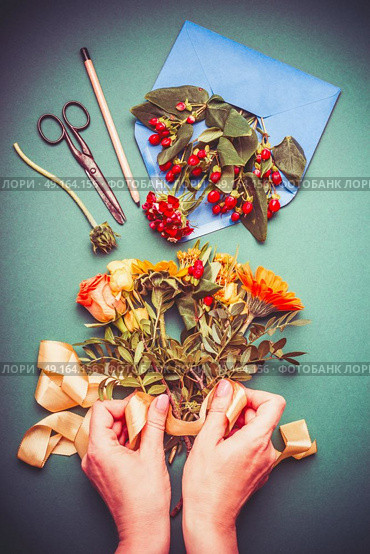 Female hand making autumn flowers arrangements on table workspace with scissors , envelope and ribbon, top view. Стоковое фото, агентство Ingram Publishing / Фотобанк Лори