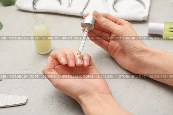 Female hands applying cuticle oil onto fingernails on grey grunge background, closeup. Стоковое фото, фотограф Pixel_shot / Фотобанк Лори