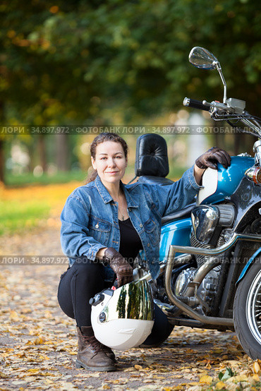 Female motorcycle rider with white crash helmet in hand sitting near her blue bike. Стоковое фото, фотограф Кекяляйнен Андрей / Фотобанк Лори