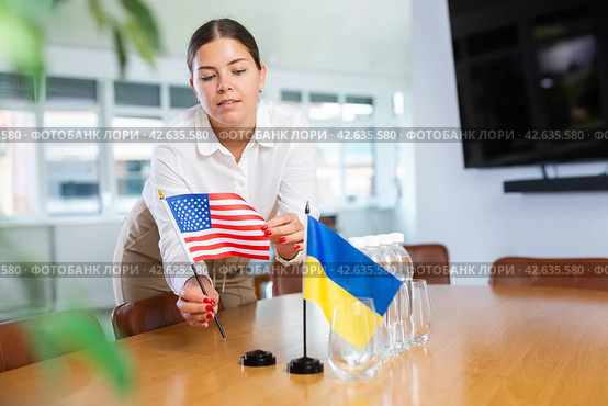 Female office coordinator placing flags of Ukraine and United States on table. Стоковое фото, фотограф Яков Филимонов / Фотобанк Лори