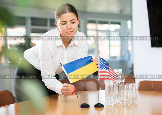 Female office coordinator placing flags of Ukraine and United States on table. Стоковое фото, фотограф Яков Филимонов / Фотобанк Лори