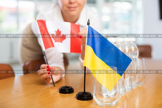 Female office coordinator setting flags of Ukraine and Canada on table. Стоковое фото, фотограф Яков Филимонов / Фотобанк Лори