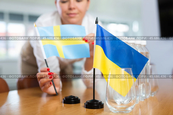 Female office coordinator setting flags of Ukraine and Sweden on table. Стоковое фото, фотограф Яков Филимонов / Фотобанк Лори