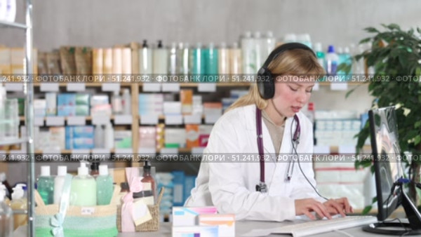Female pharmacist in headphones is talking with patient - checking data on a computer. Стоковое видео, видеограф Яков Филимонов / Фотобанк Лори