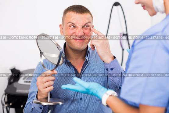 Female specialist is analysing skin of patient with using mirror before the procedure. Стоковое фото, фотограф Яков Филимонов / Фотобанк Лори