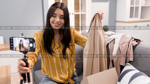 female vlogger home with smartphone unboxing clothes. Стоковое фото, агентство Ingram Publishing / Фотобанк Лори