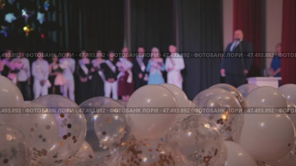 Festive white and transparent balloons scattering gold and silver confetti across graduation stage backdrop. Стоковое видео, видеограф Mikhail Davidovich / Фотобанк Лори