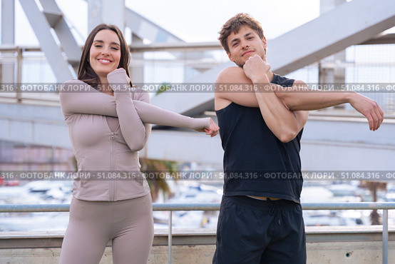 Fit couple stretching arms outdoors before workout on urban bridge. Стоковое фото, фотограф Raquel Corcoles Mendez / Фотобанк Лори