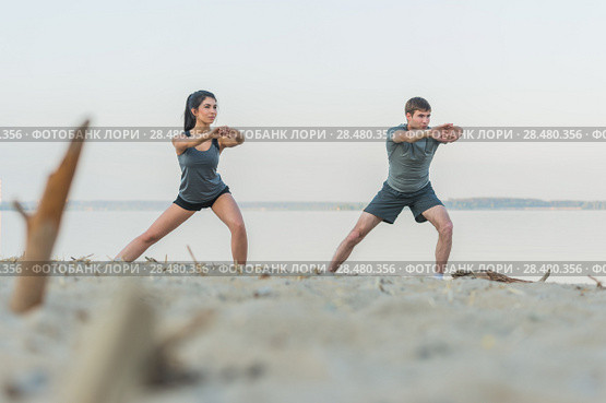 Fitness, sport, friendship and lifestyle concept - smiling couple making stretching yoga exercises on beach at morning. Стоковое фото, фотограф Kirill Kedrinskiy / Ingram Publishing / Фотобанк Лори