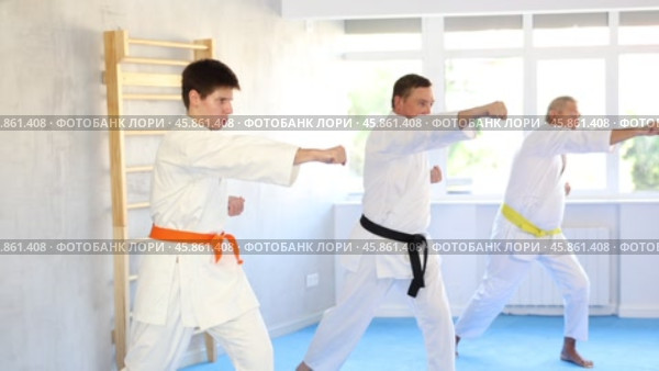 Focused beginner young judo fighter in kimono standing in attacking stance, practicing punches or hand striking techniques as part of kata with group of men. Стоковое видео, видеограф Яков Филимонов / Фотобанк Лори