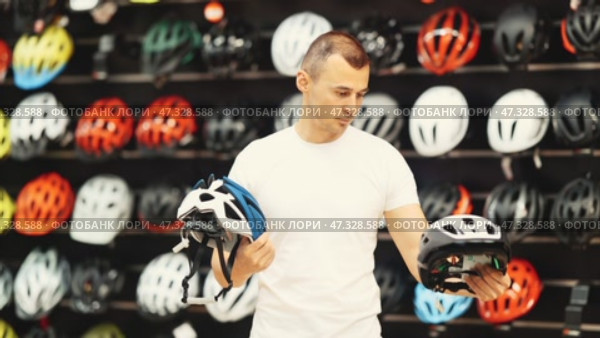 Focused interested male cyclist choosing new bicycle helmet in sports store specializing in cycling gear, comparing design and safety features of two models. Стоковое видео, видеограф Яков Филимонов / Фотобанк Лори
