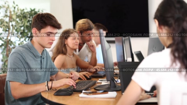 Focused young guy studying in computer lab with fellow students engrossed in coursework. Стоковое видео, видеограф Яков Филимонов / Фотобанк Лори