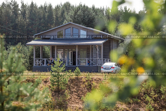 Frame house in Scandinavian style. The landscape. Quiet rest. The concept of glamping and chalet rentals. Wooden house with a veranda in nature. (2024 год). Стоковое фото, фотограф Photojuli / Фотобанк Лори