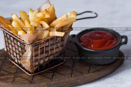 French fries in a metal basket with salt and ketchup on a stylish board on a concrete kitchen table. Fried potatoes. The concept of fast food and junk food. Стоковое фото, фотограф Photojuli / Фотобанк Лори