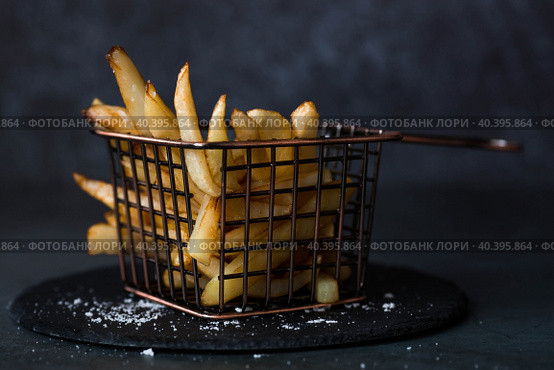 French fries in a metal basket with salt on a stylish board on a dark background. Fried potatoes. The concept of fast food and junk food. Стоковое фото, фотограф Photojuli / Фотобанк Лори