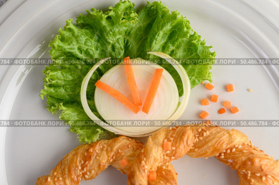 Freshly baked soft pretzel with generous sprinkling of coarse salt and sesame on white dish, decorate with lettuce and carrot beautifully, copy space. Стоковое фото, агентство Ingram Publishing / Фотобанк Лори