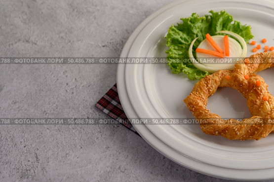 Freshly baked soft pretzel with generous sprinkling of coarse salt and sesame on white dish, decorate with lettuce and carrot beautifully, copy space. Стоковое фото, агентство Ingram Publishing / Фотобанк Лори