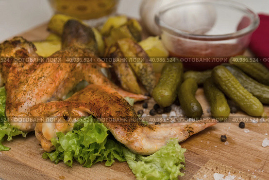 Fried chicken wings served on a wooden Board with Idaho potatoes, pickled gherkins and fresh lettuce leaves. A mug of beer is next to it. жареные куриные крылышки подаются на деревянной доске с картофелем Айдахо, маринованными корнишонами и свежими листьями салата. Рядом с ним стоит кружка пива. Стоковое фото, фотограф Дмитрий Березнев / Фотобанк Лори