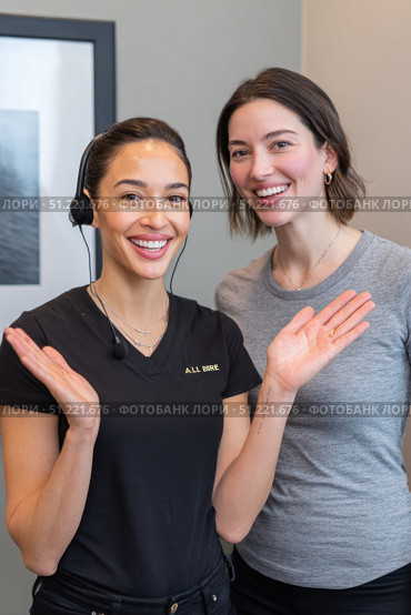 Friendly businesswomen wearing headsets communicating, smiling, and using hand gestures during professional workplace interaction with collaborative energy. Стоковое AI-изображение, AI-художник Юрий Поздников / Фотобанк Лори