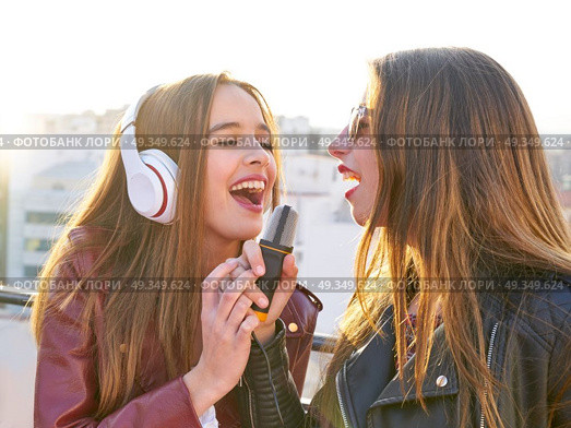 friends band firls singing karaoke at roof terrace. Best friends band girls singing karaoke outdoor at roof terrace in the city. Стоковое фото, агентство Ingram Publishing / Фотобанк Лори