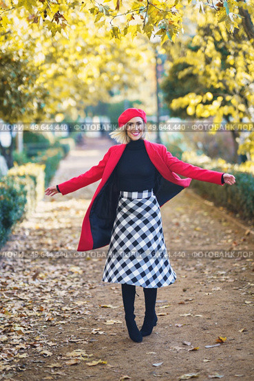 Full body of cheerful female in red coat and beret looking at camera while spinning around on walkway in autumn park. Happy woman spinning around on pathway. Стоковое фото, агентство Ingram Publishing / Фотобанк Лори