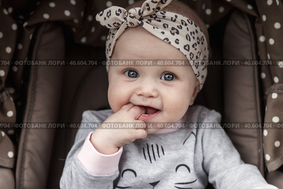 Funny pensive baby with blue eyes sitting in stroller, sad looking at camera. Adorable bored cute child infant with fingers in mouth in pram. Concept of infancy, childhood emotion. Copy ad text space. Стоковое фото, фотограф Aleksandr Golubev / Фотобанк Лори