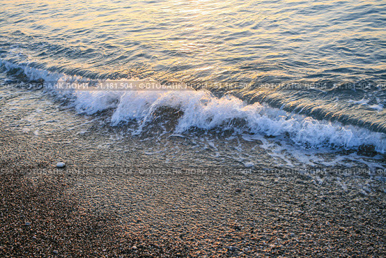 Gentle sea waves lapping against a pebbled shore during a serene sunset atmosphere. Стоковое фото, фотограф Наталья Семкина / Фотобанк Лори