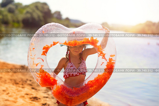 Girl in a hat stands on the river bank with a transparent inflatable circle in the shape of a heart with orange feathers inside. Beach holidays, swimming, tanning, sunscreens. Стоковое фото, фотограф Ольга Симонова / Фотобанк Лори