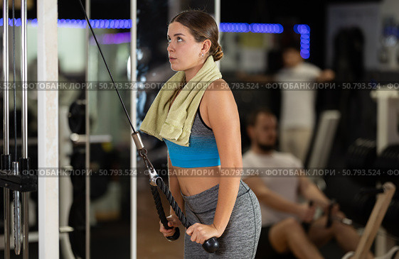 Girl in gym performs exercises for arm muscles using cable machine and pull weighted rope. Стоковое фото, фотограф Яков Филимонов / Фотобанк Лори