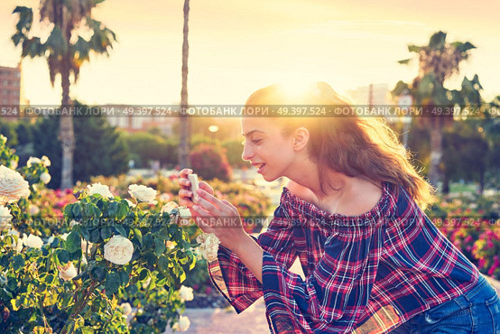Girl portrait taking photos to a rose flower with smarphone. Стоковое фото, агентство Ingram Publishing / Фотобанк Лори