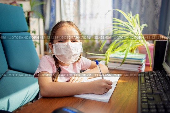 Girl schoolgirl in a medical mask does homework in front of a computer. Quarantine and home schooling. Стоковое фото, фотограф Екатерина Кузнецова / Фотобанк Лори
