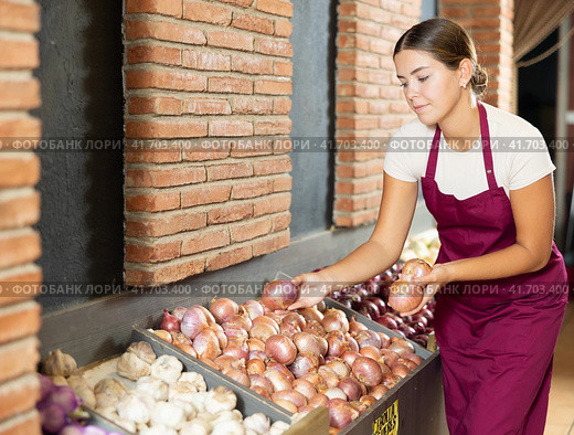 Girl seller of garden stuff store is replenishing showcase with vegetables, puts onion on showcase. Стоковое фото, фотограф Яков Филимонов / Фотобанк Лори