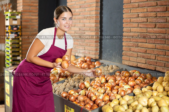 Girl seller of garden stuff store is replenishing showcase with vegetables, puts onion on showcase. Стоковое фото, фотограф Яков Филимонов / Фотобанк Лори