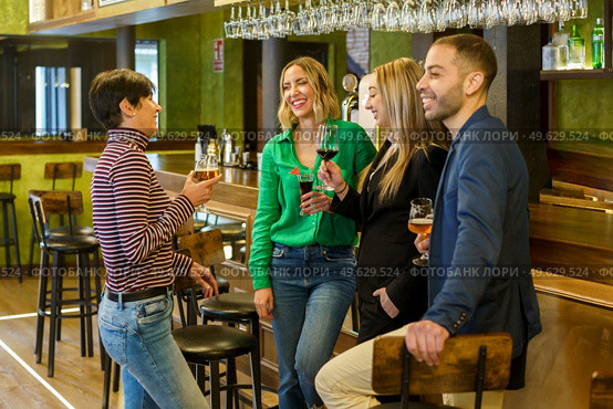 Gleeful diverse man and women with alcohol beverages smiling and talking while spending weekend day in bar together. Happy friends chatting in a beautiful bar. Стоковое фото, агентство Ingram Publishing / Фотобанк Лори