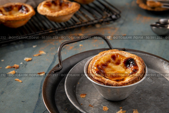 Golden-brown Portuguese custard tart on a rustic metal tray with a wire rack in the background. Стоковое фото, агентство Ingram Publishing / Фотобанк Лори