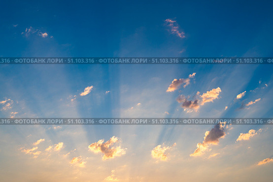 Golden sunbeams are radiating through scattered clouds, creating a mesmerizing spectacle in the vast expanse of the twilight sky during a breathtaking sunset. Стоковое фото, фотограф Ольга Ильина / Фотобанк Лори