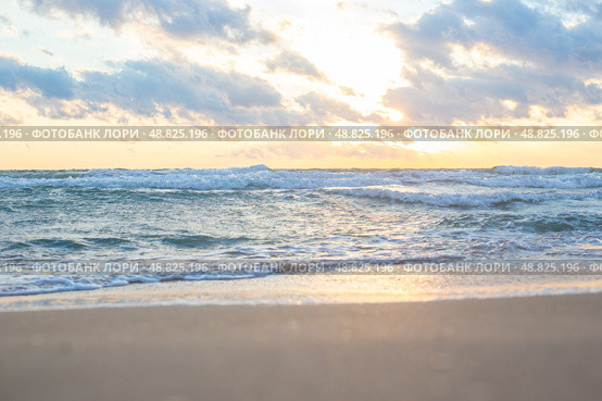 Golden sunlight shining through clouds over calm ocean with soft waves lapping at sandy beach. Стоковое фото, фотограф Коханова Наталья / Фотобанк Лори