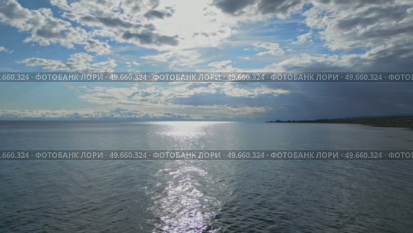 Голубая вода озера Иссык-Куль, отражение солнца. Солнечный свет сквозь белые облака, летний день. Главная туристическая достопримечательность Кыргызстан. Горы вдалеке. Съемка с воздуха с дрона (2023 год). Стоковое видео, видеограф Екатерина Якименко / Фотобанк Лори
