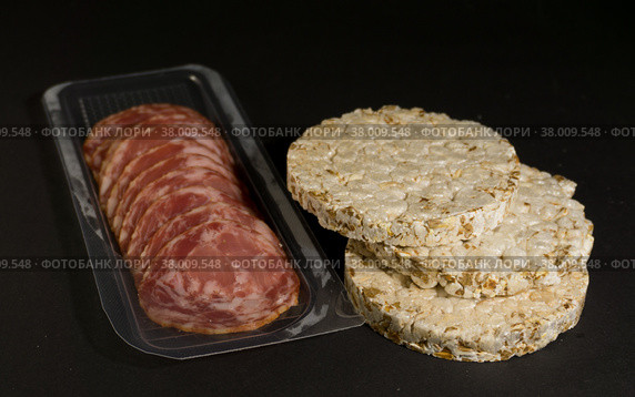 Grain crispbreads crispy rice and diet bread with smoked sausage. Rice cake puffed rice with salami, sausage, balyk, smoked meat on black background. Стоковое фото, фотограф Tae Mi / Фотобанк Лори