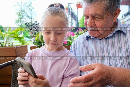 Granddaughter showing smartphone to grandfather. Portrait of a cute girl playing or typing on her smartphone while sitting in a cafe with her grandfather. Стоковое фото, фотограф Терехова Марина / Фотобанк Лори