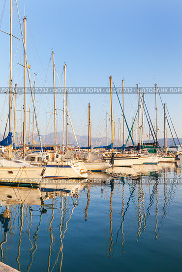 Greece. Crete. Beautiful seascape with yachts in marina of Agios Nikolaos in setting sun. The masts of the yachts are reflected in the blue water of the Mirabello Bay. Summer travel and seaside holidays (2014 год). Стоковое фото, фотограф Виктория Катьянова / Фотобанк Лори