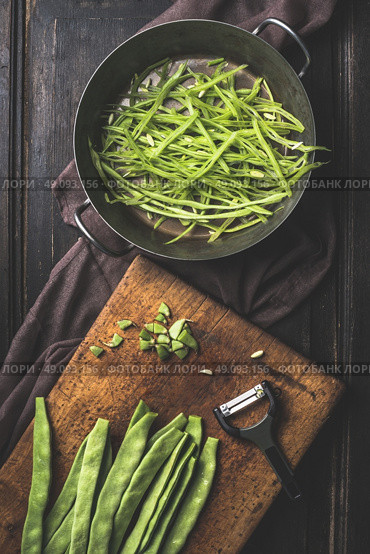 Green french beans cooking. Slices  Green french beans in cooking pot and vegetable peeler on dark rustic wooden background, top view. Стоковое фото, агентство Ingram Publishing / Фотобанк Лори