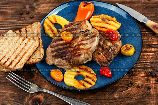 Grilled meat with pineapple rings, grilled steak and ananas on wooden table.. Pork steak with pineapple on plate. Стоковое фото, агентство Ingram Publishing / Фотобанк Лори