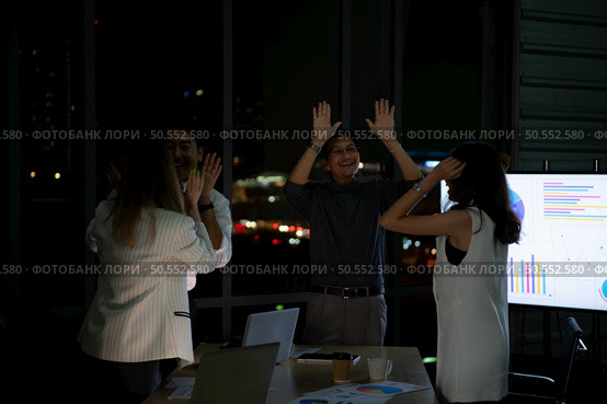 Group of broker international stock traders working actively at night in office, Everyone is congratulating the team on their success. Стоковое фото, агентство Ingram Publishing / Фотобанк Лори