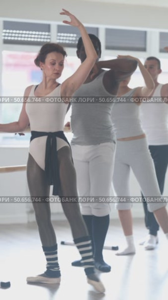 Group of concentrated amateur ballet enthusiasts practicing combination of forward and side battement tendu with arms in third position at barre, improving posture and grace in sunlit mirrored studio. Стоковое видео, видеограф Яков Филимонов / Фотобанк Лори