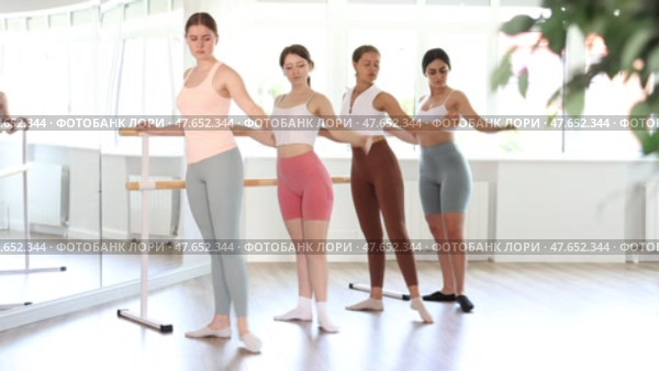Group of enthusiastic young female ballet students focused on mastering graceful Demi rond de jambe par terre exercise at barre in mirrored well-lit choreography studio. Стоковое видео, видеограф Яков Филимонов / Фотобанк Лори