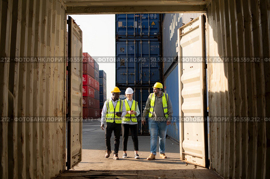 Group of workers in an empty container storage yard, The condition of the old container is being assessed to determine whether it requires maintenance for usage. Стоковое фото, агентство Ingram Publishing / Фотобанк Лори