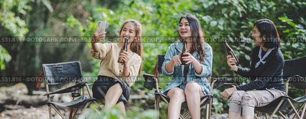 Group of young asian women drink beer in their chairs and soaked their feet in the stream while camping in the nature park, They are enjoy to talking and laugh fun together. Стоковое фото, агентство Ingram Publishing / Фотобанк Лори