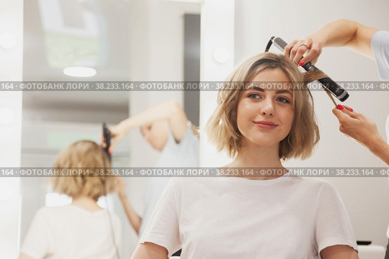 Hairdresser does hairstyle cute pretty young woman in beauty salon. Customer service in interior room create an amazing image. Work hairstyles creation wizard. Concept style, satisfaction. Copy space. Стоковое фото, фотограф Aleksandr Golubev / Фотобанк Лори