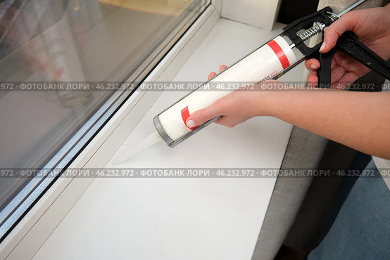 Hand applying sealant to window sill using caulking gun. Home renovation and window maintenance concept. Стоковое фото, фотограф Андрей Журавлев / Фотобанк Лори